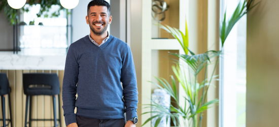 A man smiling, stood in a modern office